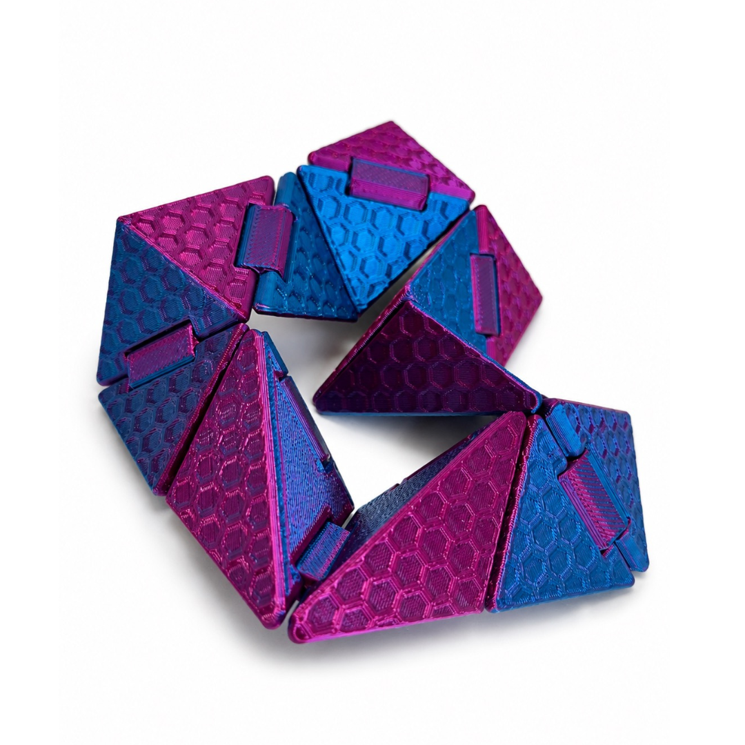 Cubigami cubo geométrico articulado con acabado metálico magenta y azul sobre fondo blanco minimalista.